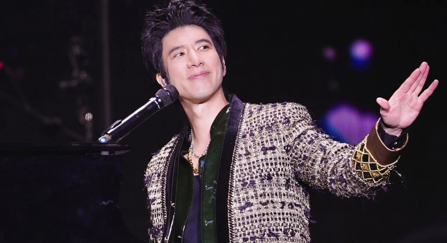An onstage moment featuring Wang Leehom at the piano, wearing an embellished jacket under concert lighting