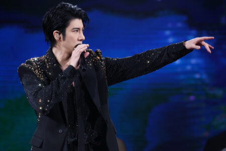 Wang Leehom in a black sequined blazer pointing dramatically while performing with blue and green stage lighting