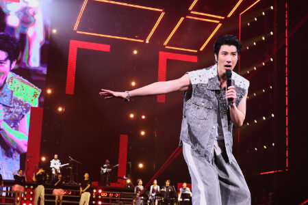 Wang Leehom in a sleeveless denim vest performing with geometric orange neon lighting patterns in the background